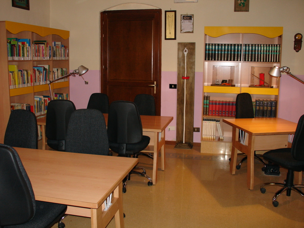 Sala interna della sezione ragazzi della biblioteca comunale, tavoli, sedie e scaffali con i libri sulle pareti
